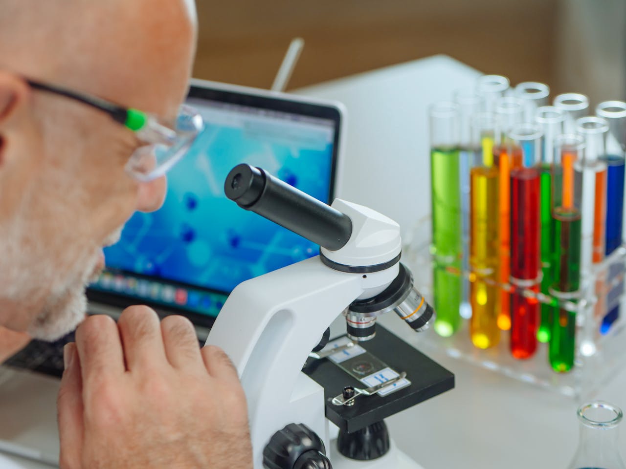 Scientist using microscope with colorful test tubes in a modern laboratory setting.