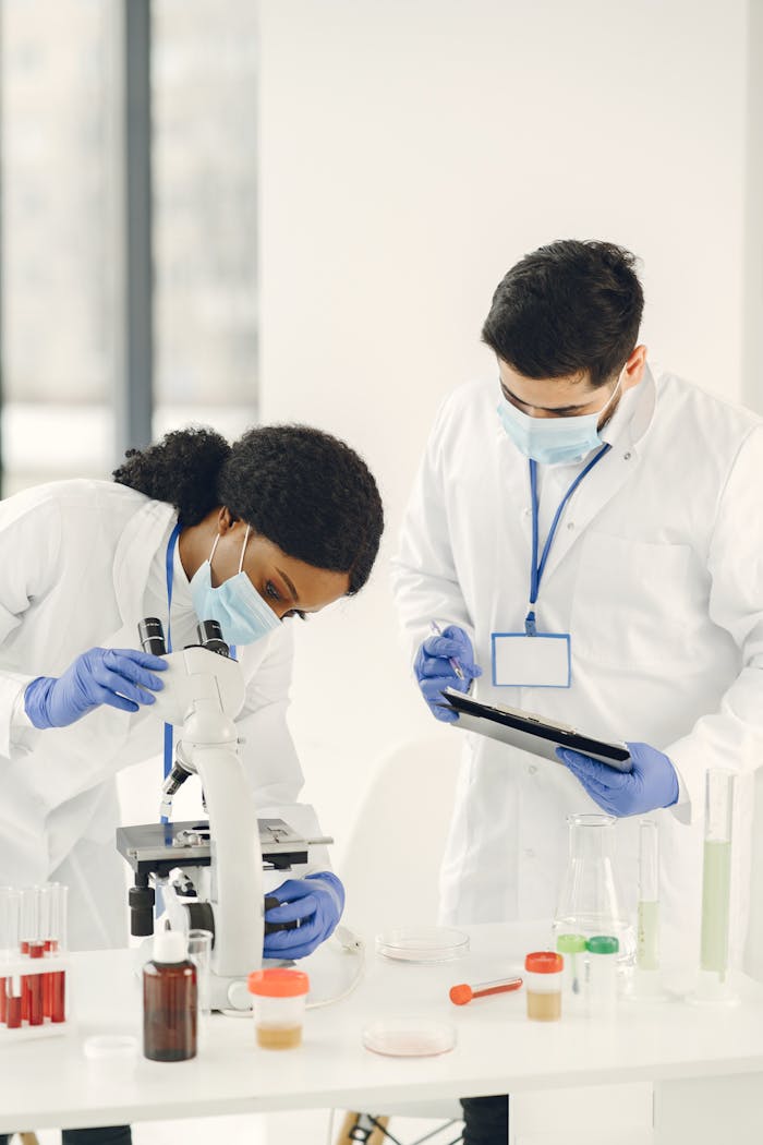 Two scientists in lab coats examining samples using a microscope, highlighting teamwork in research.